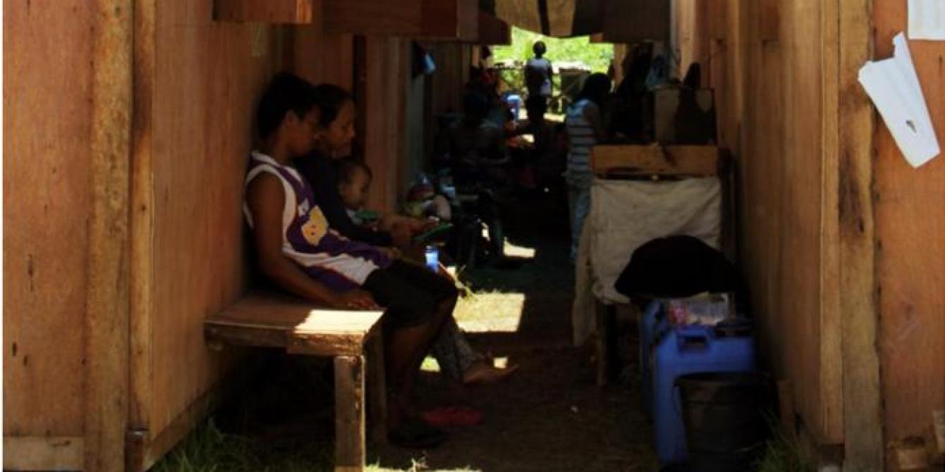 A family sits outside the bunkhouse where they continue to live after being displaced by typhoon Haiyan. Many of those in bunkhouses are being targeted for permanent resettlement to safer land as part of recovery plans. Photo: Genevive Estacaan/Oxfam 2014